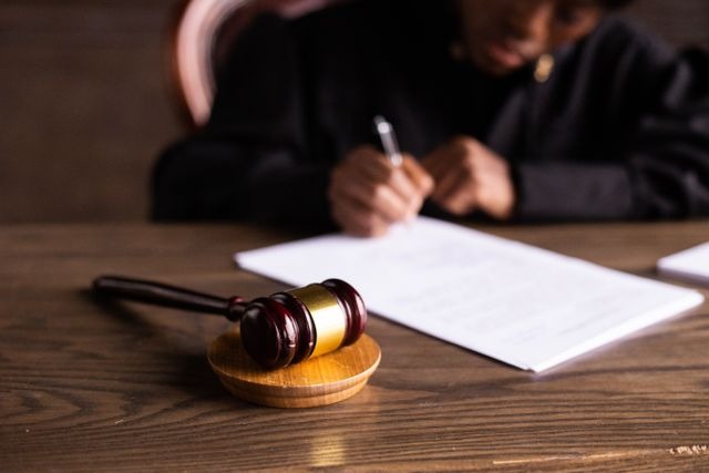 a judge writing at their desk behind a wooden gavel