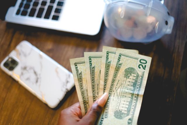 A New Jersey property owner budgeting with a phone a laptop a piggy bank and cash