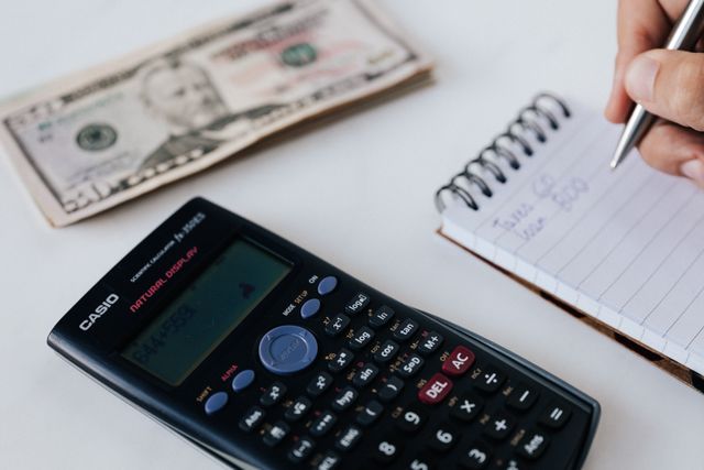 A property owner using a calculator and notepad next to a stack of bills